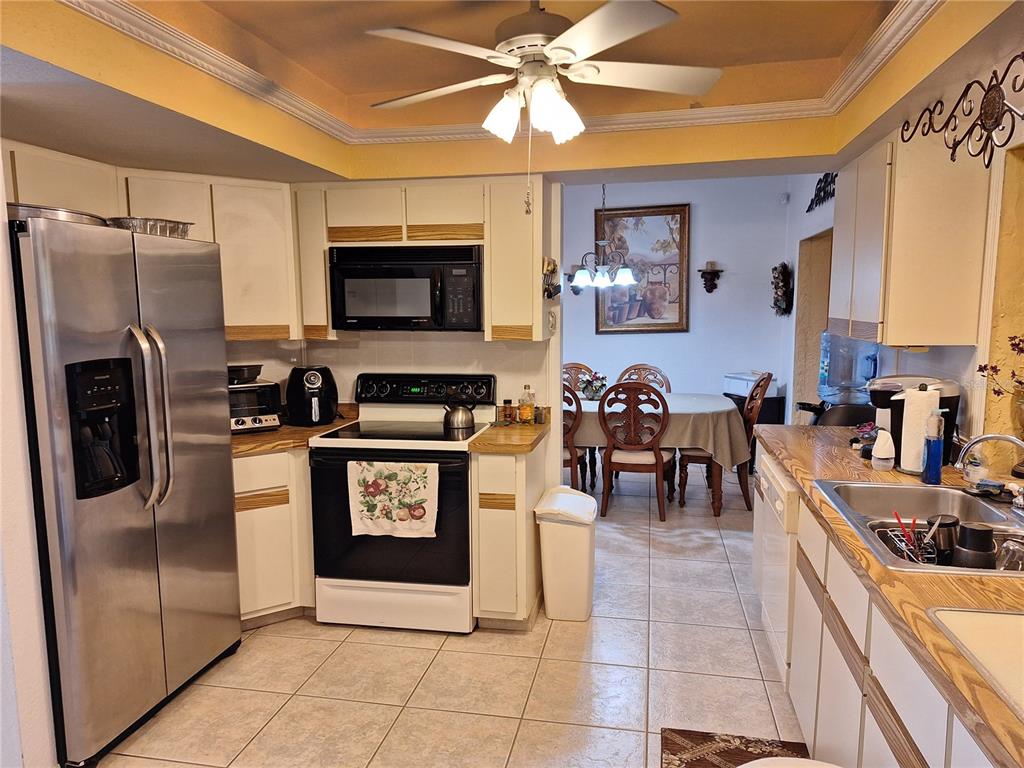 A kitchen with white cabinets, stainless steel appliances, and tile flooring opens to a dining area — 2223 TINKER STREET, PORT CHARLOTTE, FL