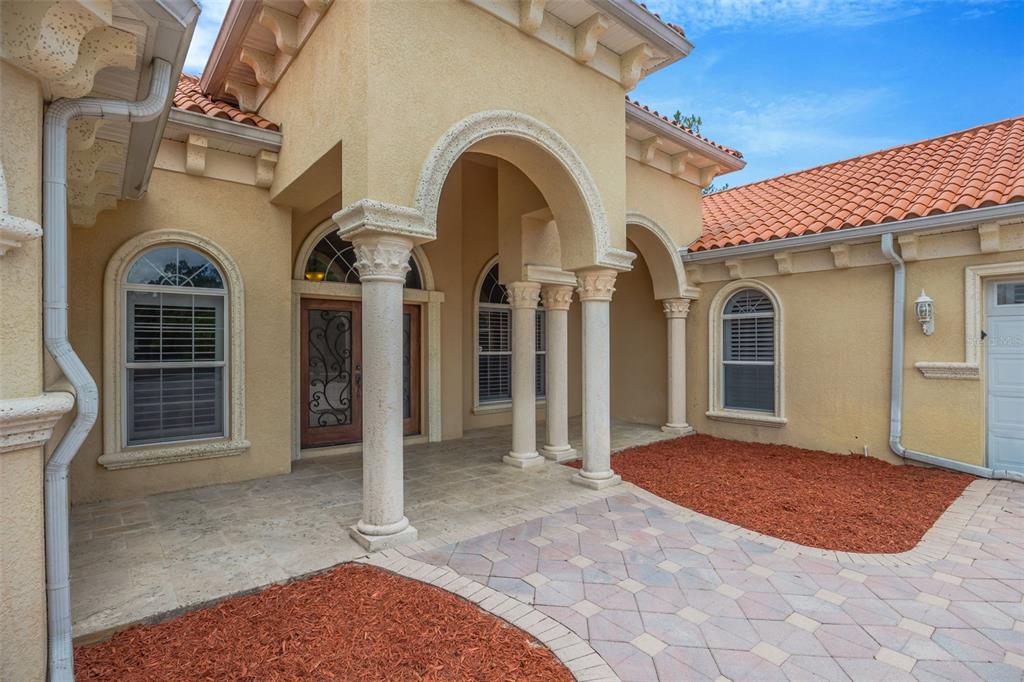 The exterior of a stucco home features a covered entryway with columns and arched windows — 8610 VIVIAN BASS WAY, ODESSA, FL