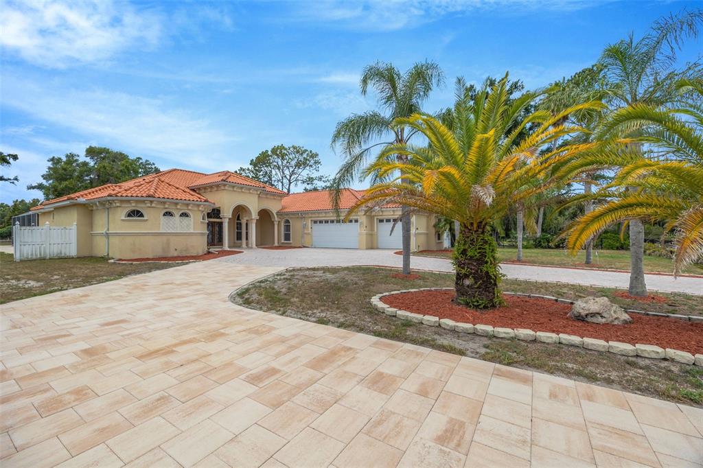 A single-story house with a tile roof, arched entryway, and a large paved driveway — 8610 VIVIAN BASS WAY, ODESSA, FL