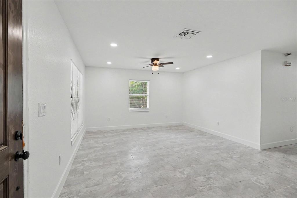 An empty room features white walls, gray tile flooring, a ceiling fan, and a window — 1128 NEVILLE AVENUE, LAKELAND, FL