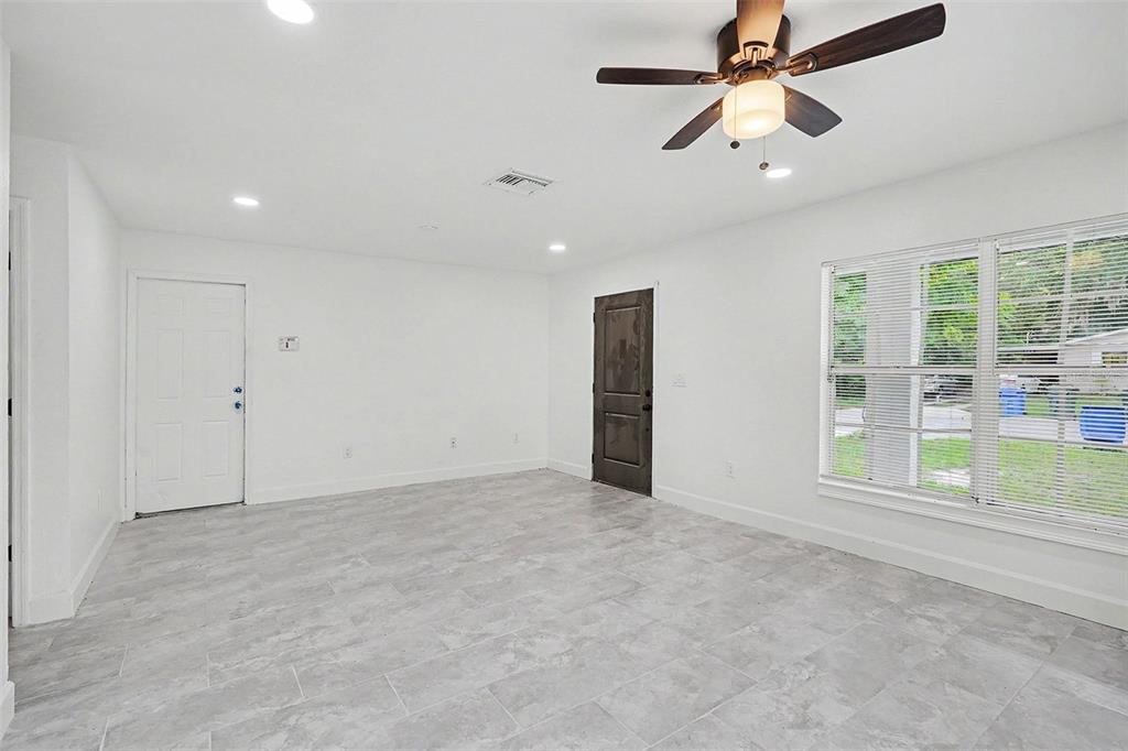 A bright, empty room features white walls, gray tile flooring, a ceiling fan, and windows — 1128 NEVILLE AVENUE, LAKELAND, FL