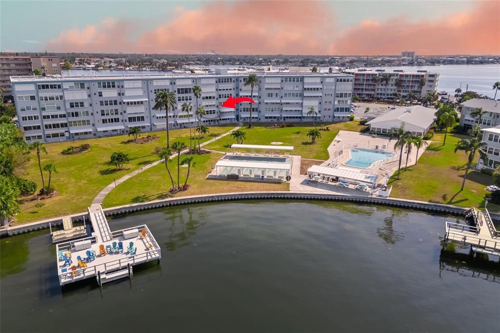 An aerial view of a waterfront apartment complex with a pool, dock, and grassy lawn — 1868 SHORE DRIVE S UNIT 207, SOUTH PASADENA, FL