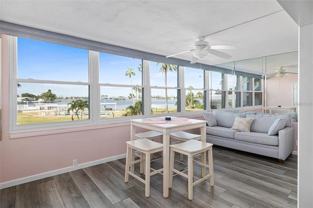 A sunroom features a dining set, a gray sofa, wood-look flooring, and waterfront views — 1868 SHORE DRIVE S UNIT 207, SOUTH PASADENA, FL