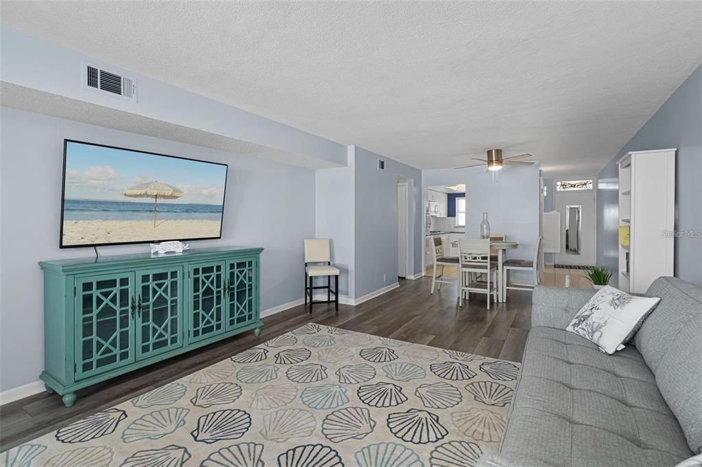 A living room with a shell-patterned rug, teal media console, and an adjacent dining area — 1868 SHORE DRIVE S UNIT 207, SOUTH PASADENA, FL
