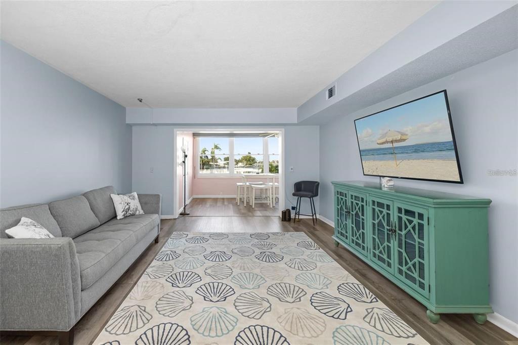 A living room features a gray sofa, a seashell-patterned rug, and a teal media console — 1868 SHORE DRIVE S UNIT 207, SOUTH PASADENA, FL