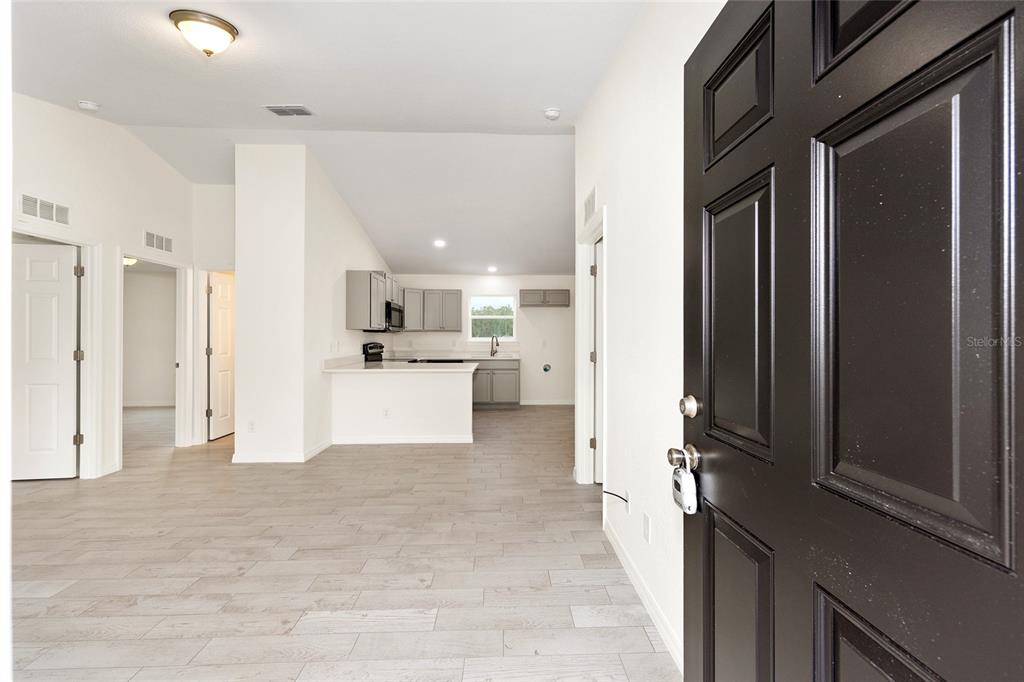 An interior view shows a foyer leading to an open-concept kitchen with light gray cabinets — 229 LOCUST LANE, OCALA, FL