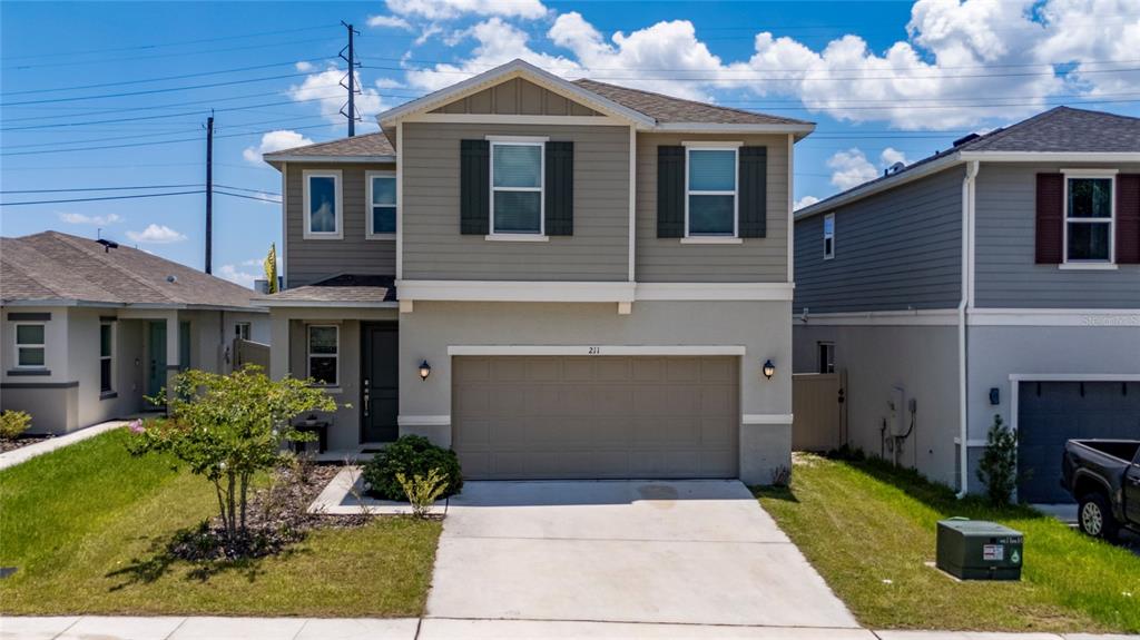 A two-story suburban house with a tan garage, beige siding, and a concrete driveway — 211 ASH WAY, AUBURNDALE, FL