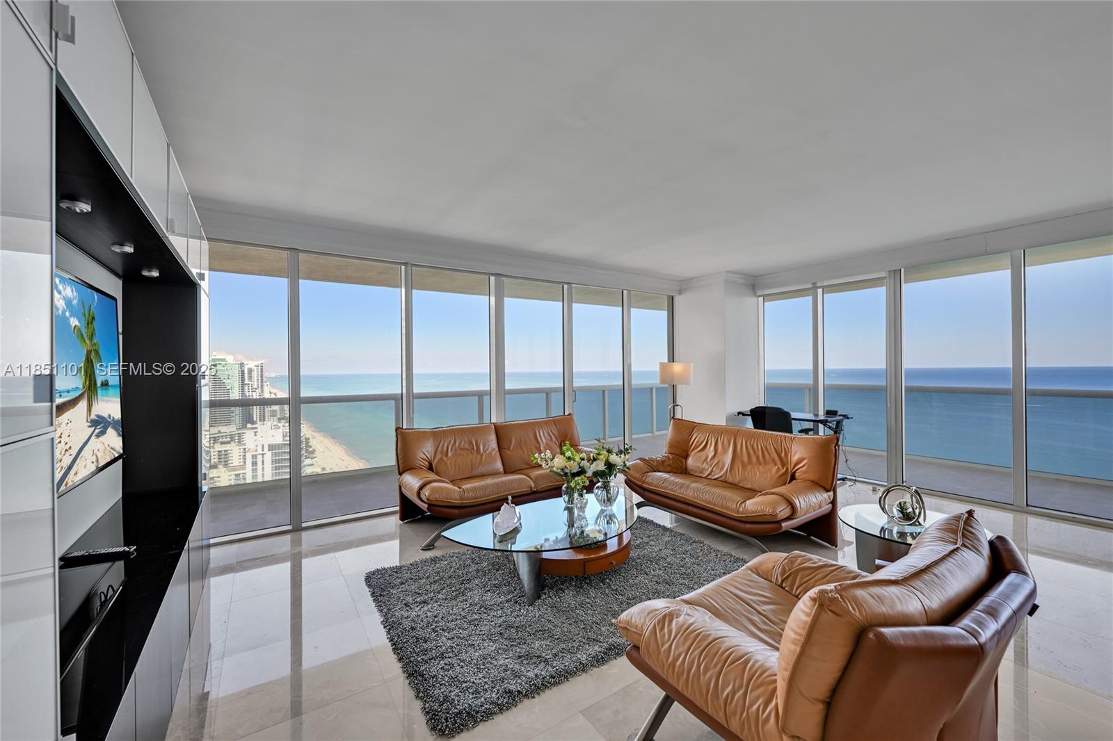 A modern living room features tan leather sofas, a glass coffee table, and floor-to-ceiling windows — 1830 S Ocean Dr # 3801, Hallandale Beach FL 33009, HALLANDALE BEACH, FL