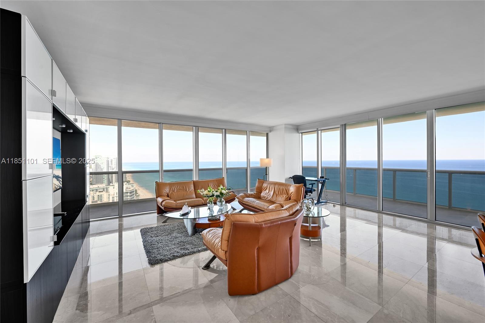 A living room features tan leather furniture, marble floors, and floor-to-ceiling windows overlooking the ocean — 1830 S Ocean Dr # 3801, Hallandale Beach FL 33009, HALLANDALE BEACH, FL