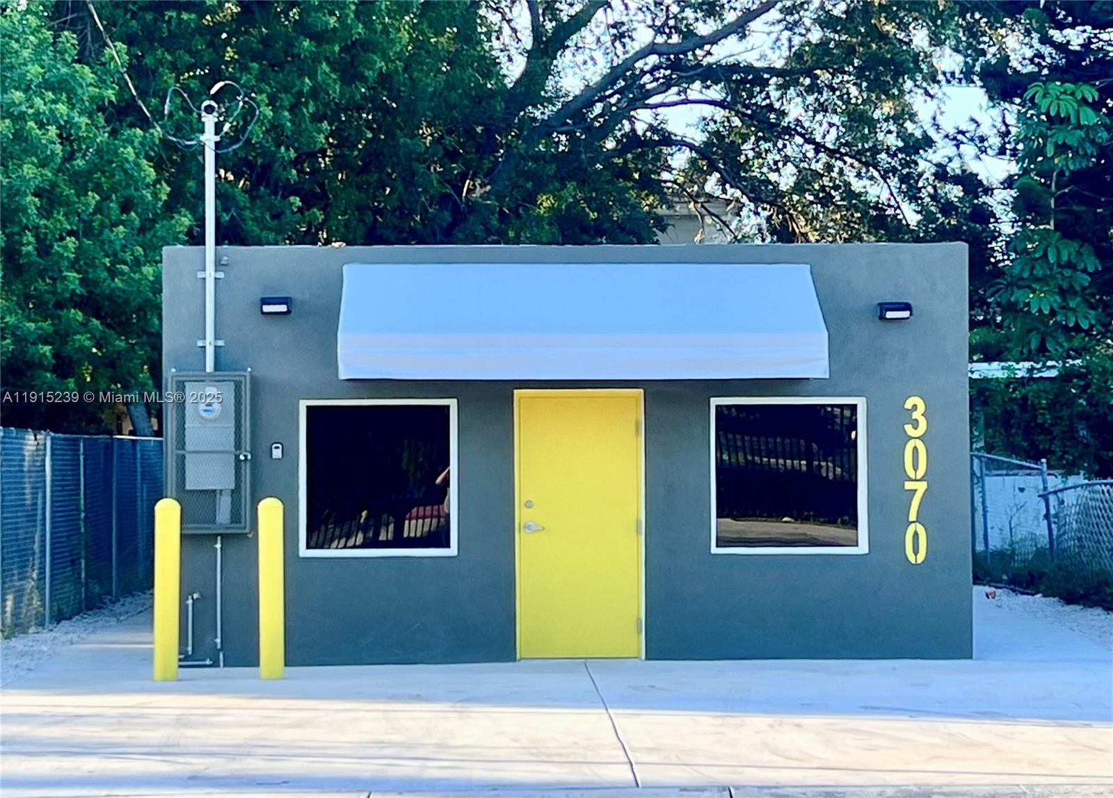 A gray exterior building features a bright yellow door, two windows, and a white awning — 3070 NW 46th St, Miami FL 33142, MIAMI, FL