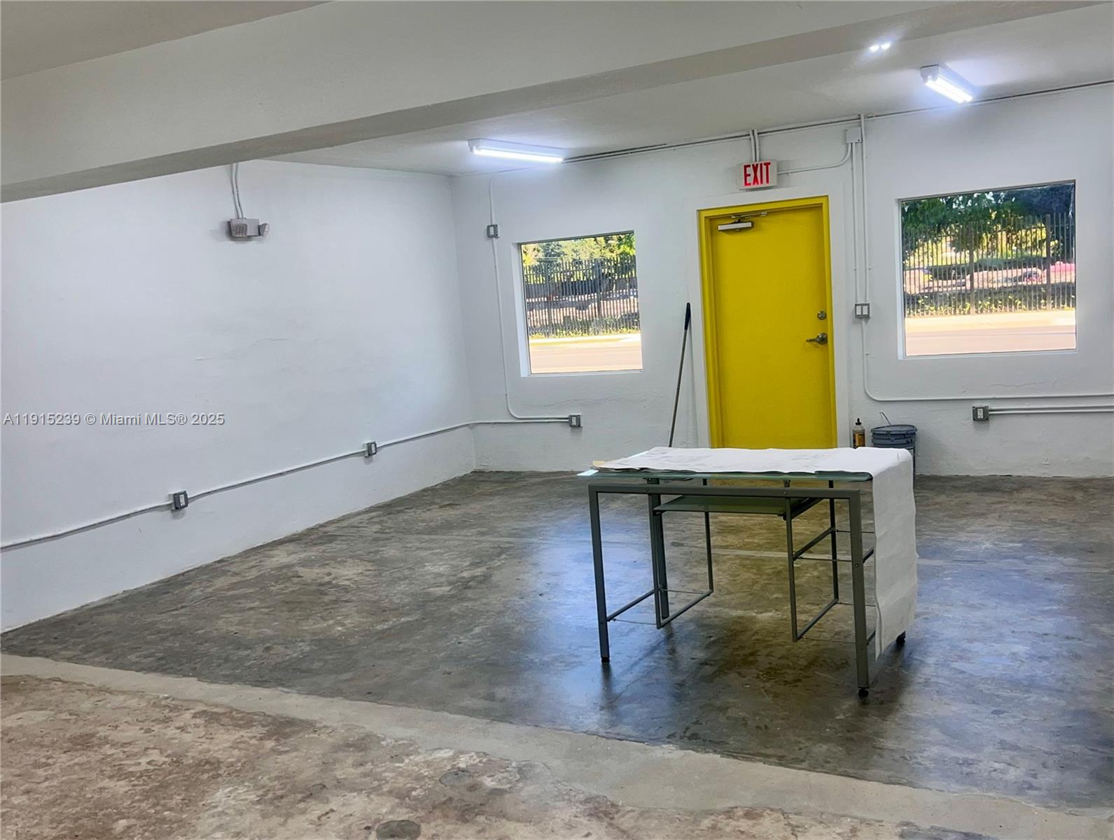 An empty room with concrete floors, white walls, a yellow door, and a glass table — 3070 NW 46th St, Miami FL 33142, MIAMI, FL