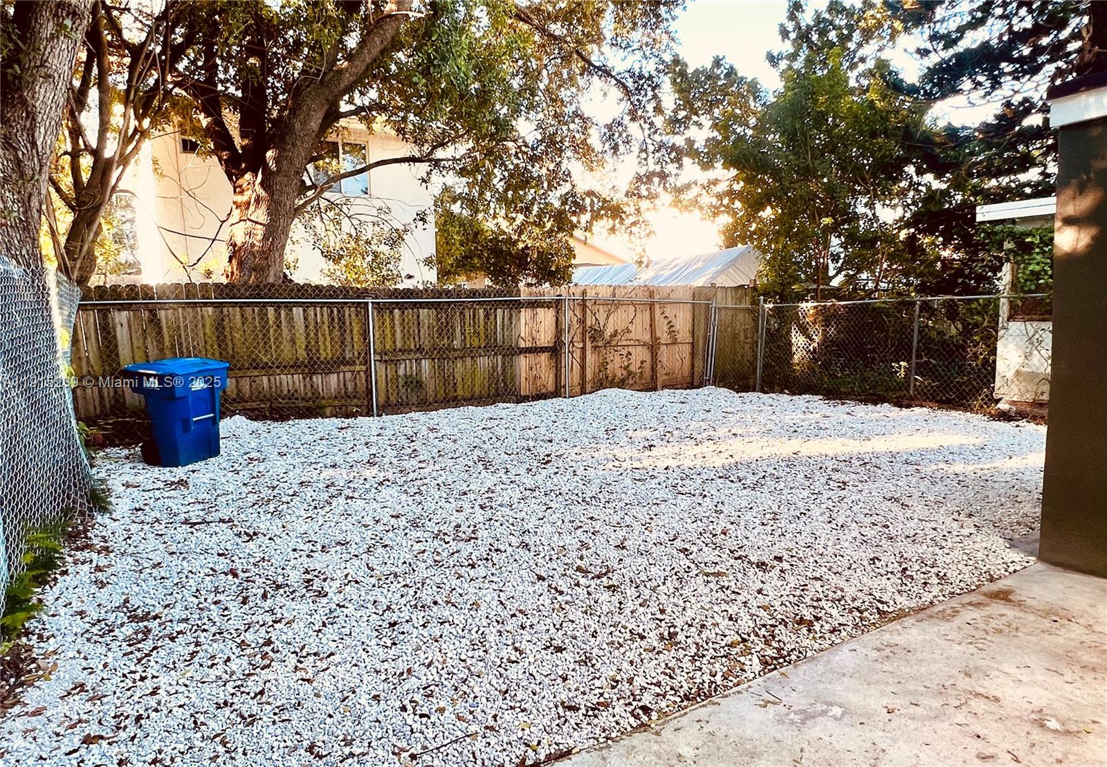 A fenced backyard features a gravel ground cover and a blue trash bin — 3070 NW 46th St, Miami FL 33142, MIAMI, FL