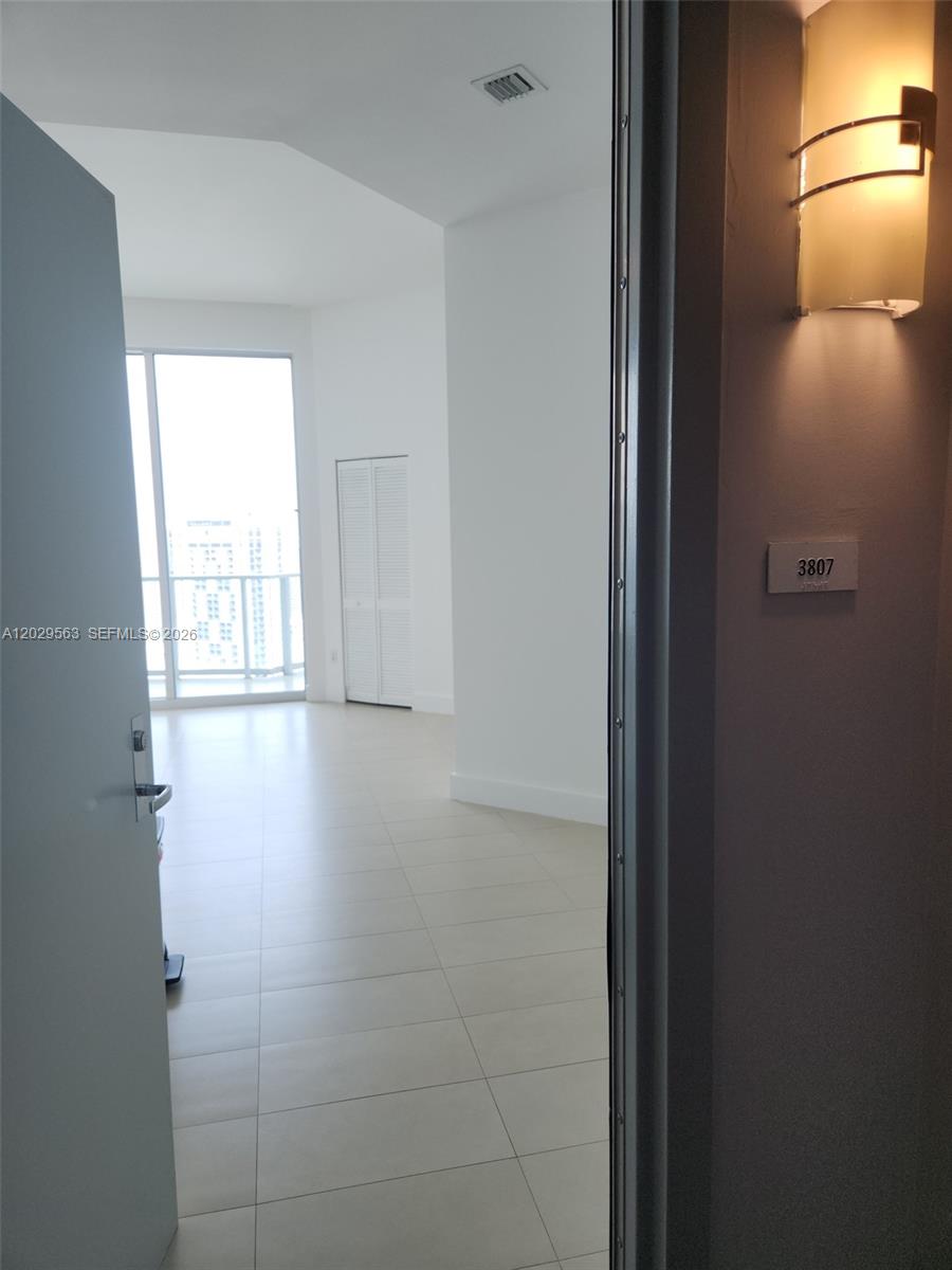 A view through an open doorway into a bright, tiled apartment with a balcony — 300 S Biscayne Blvd # 3807, Miami FL 33131, MIAMI, FL