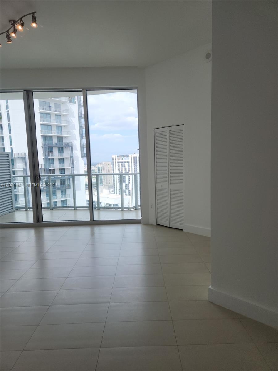An empty room with light tile floors, a white closet, and floor-to-ceiling windows overlooking buildings — 300 S Biscayne Blvd # 3807, Miami FL 33131, MIAMI, FL