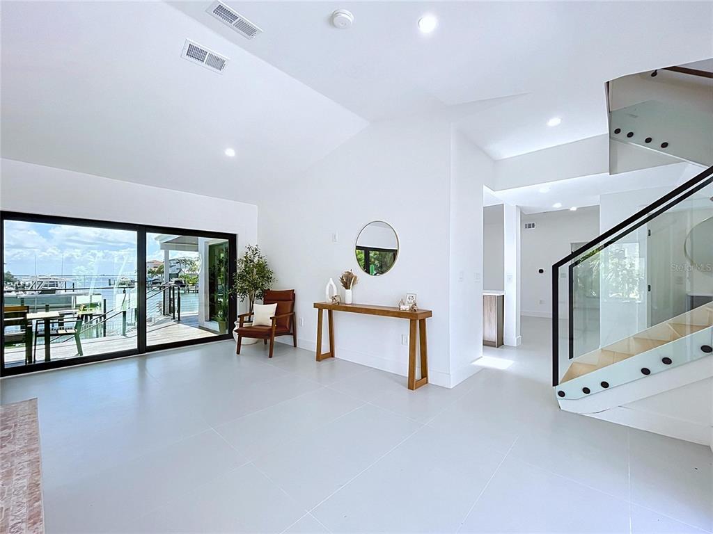A bright, modern living area features white tile floors, a glass staircase, and sliding glass doors — 807 2ND AVENUE S, TIERRA VERDE, FL