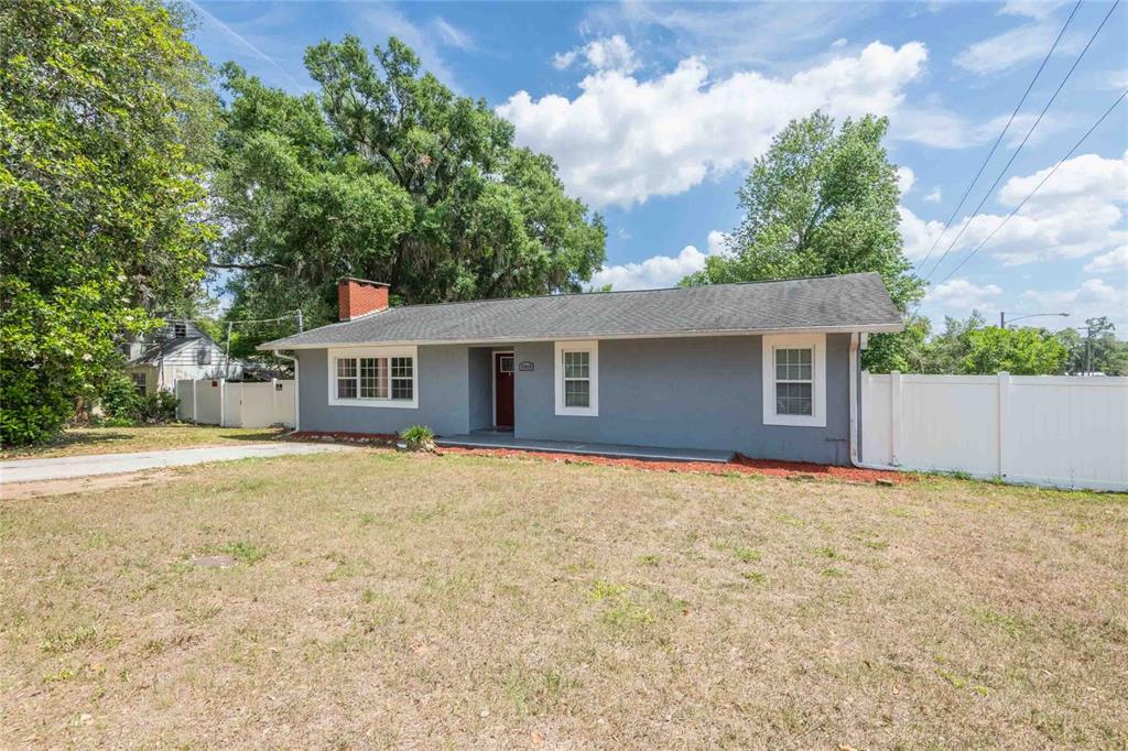 A single-story gray house with a brick chimney and a white fence sits on grass — 37010 CHURCH AVENUE, DADE CITY, FL