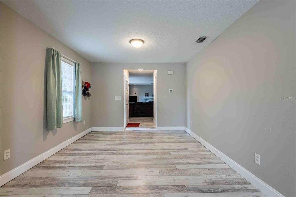 A room with light gray walls, wood-look flooring, and a doorway leading to another area — 37010 CHURCH AVENUE, DADE CITY, FL