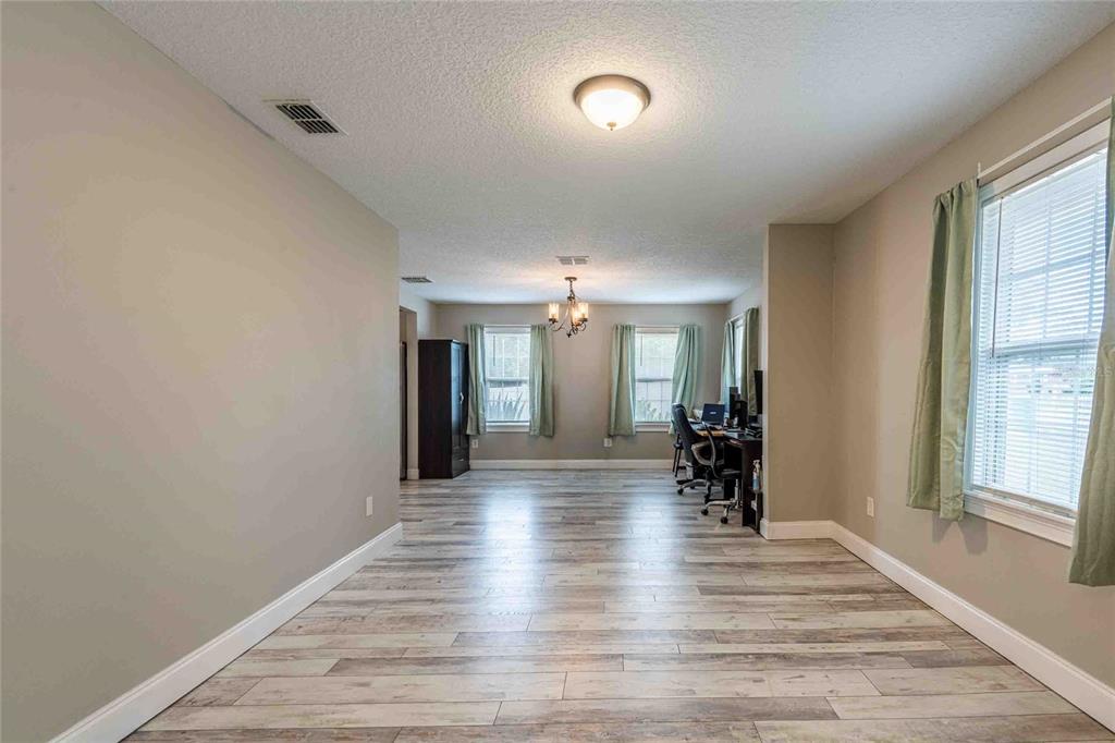 A spacious room with light wood-look flooring, neutral walls, and multiple windows with green curtains — 37010 CHURCH AVENUE, DADE CITY, FL