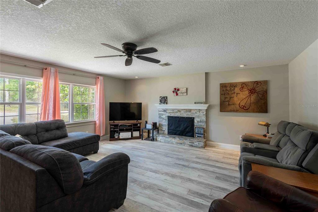 A living room features a stone fireplace, gray wood-look flooring, and two dark gray sofas — 37010 CHURCH AVENUE, DADE CITY, FL