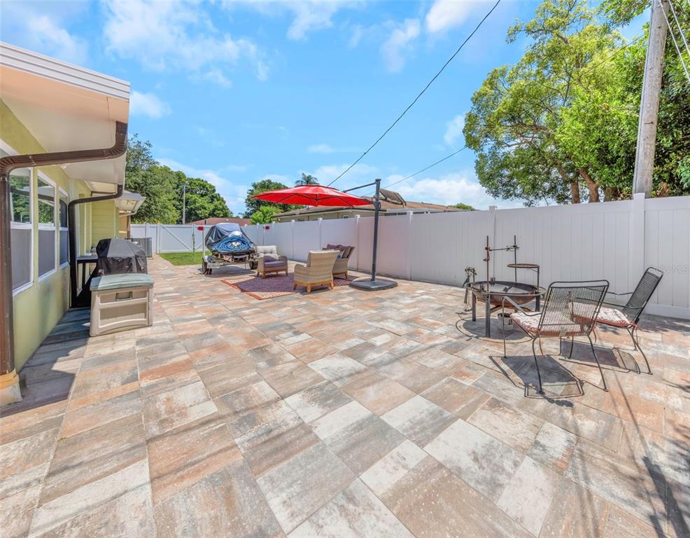 A paved backyard patio features outdoor seating, a red umbrella, and a white privacy fence — 2465 BURNICE DRIVE, CLEARWATER, FL