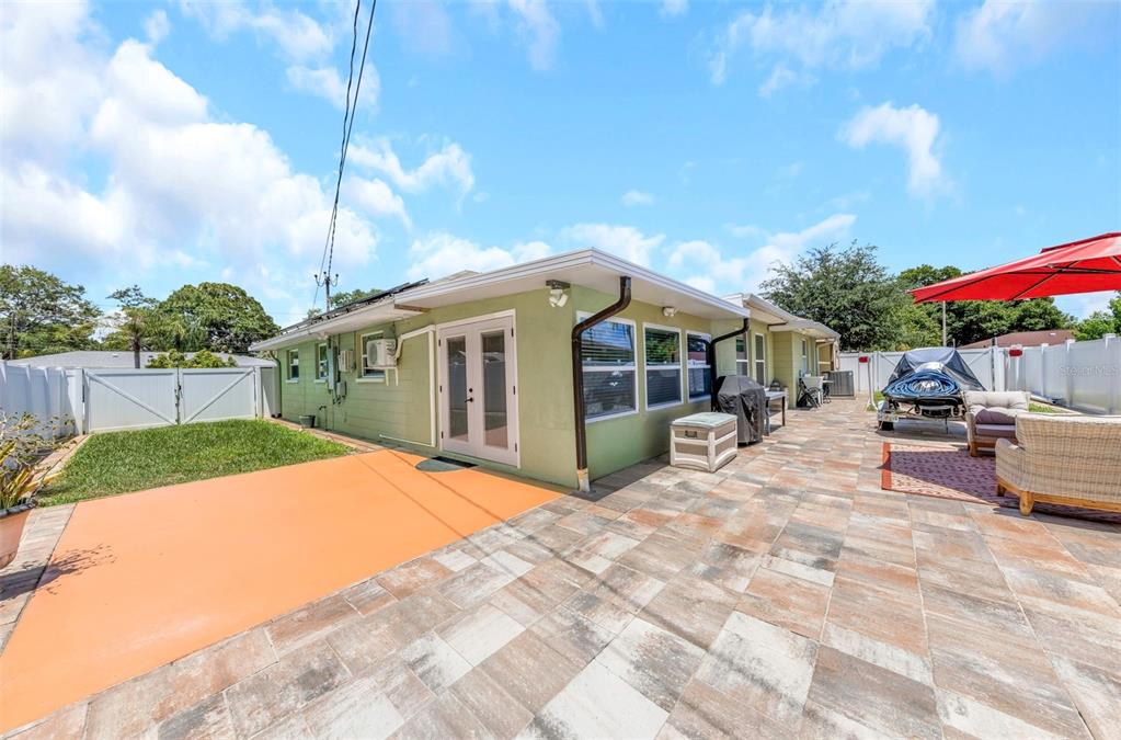 A green house exterior features a tiled patio, double glass doors, and a fenced yard — 2465 BURNICE DRIVE, CLEARWATER, FL