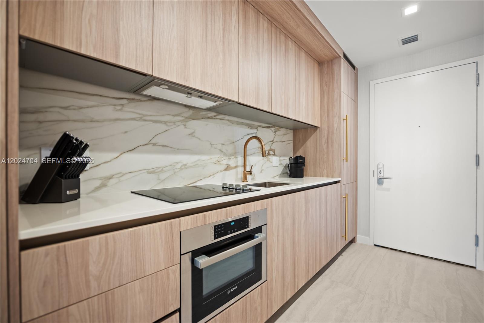 A modern kitchen features light wood cabinetry, a marble backsplash, and a built-in Bosch oven — 77 SE 5th Street # 1604, Miami FL 33131, MIAMI, FL