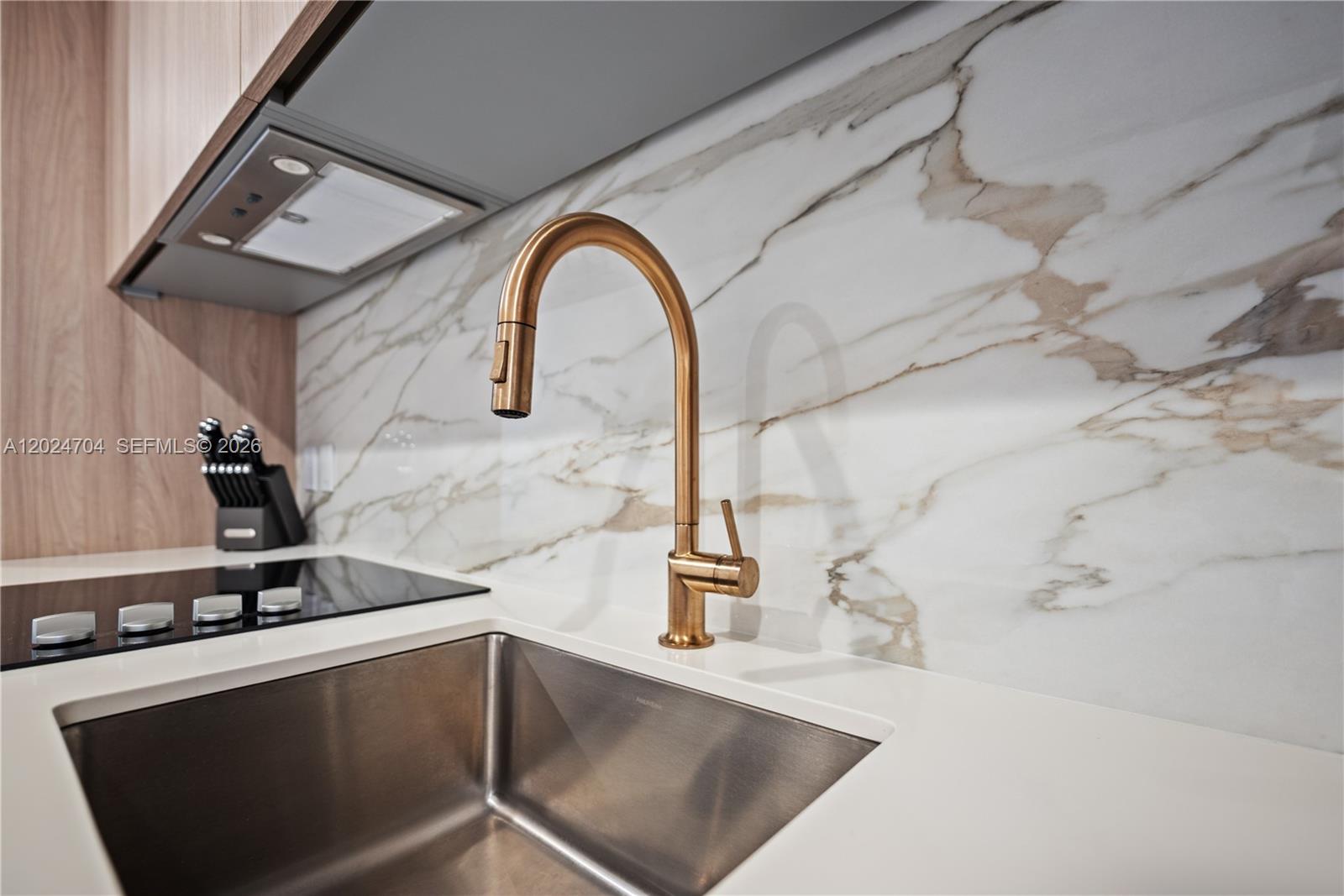 A modern kitchen features a stainless steel sink, gold faucet, and marble-patterned backsplash — 77 SE 5th Street # 1604, Miami FL 33131, MIAMI, FL