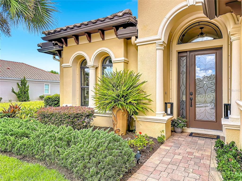 A tan stucco house exterior features a brown front door with decorative glass and landscaping — 341 HIBISCUS WAY, PALM COAST, FL