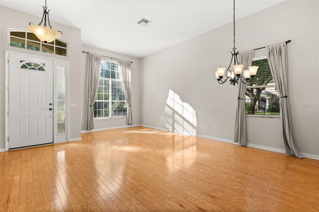 An empty room with hardwood floors, a chandelier, and large windows with curtains — 3289 RED ASH CIRCLE, OVIEDO, FL