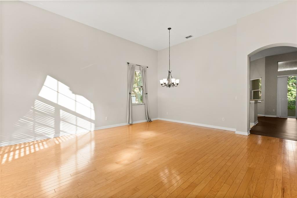 A bright, empty dining room features hardwood floors, a chandelier, and an arched entryway — 3289 RED ASH CIRCLE, OVIEDO, FL