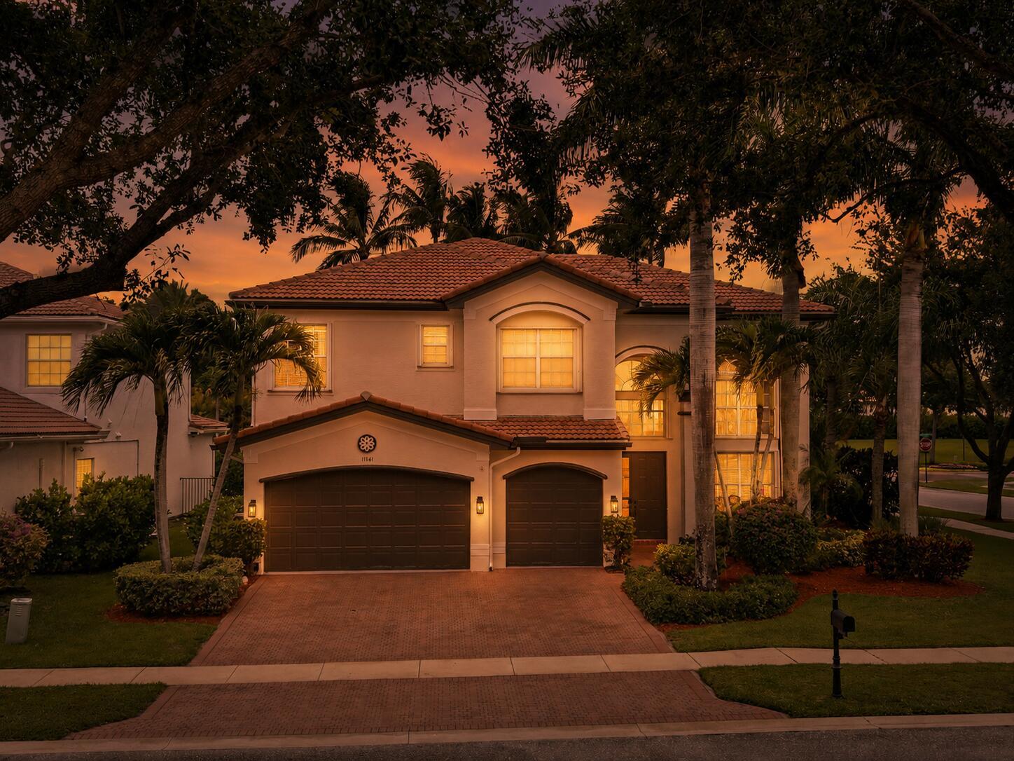 A two-story house with a tile roof, two garage doors, and palm trees at dusk — 11161 Sunset Ridge Circle, Boynton Beach FL 33473, BOYNTON BEACH, FL