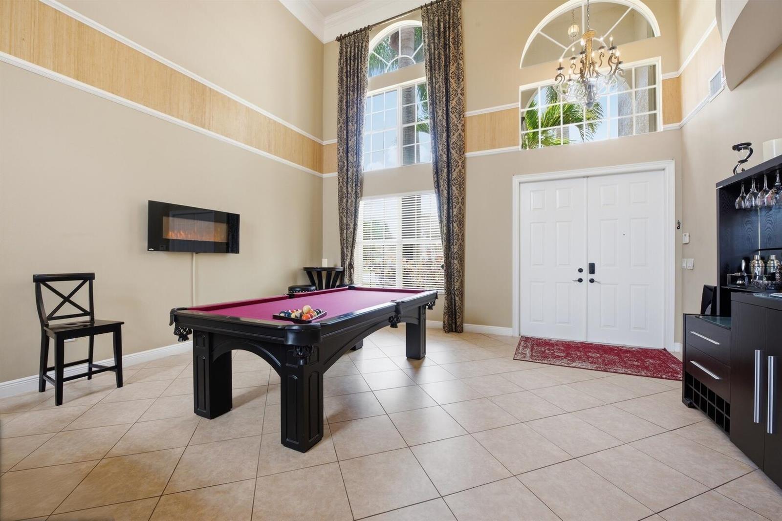 A high-ceilinged game room features a pool table, a wall-mounted fireplace, and a home bar — 11161 Sunset Ridge Circle, Boynton Beach FL 33473, BOYNTON BEACH, FL