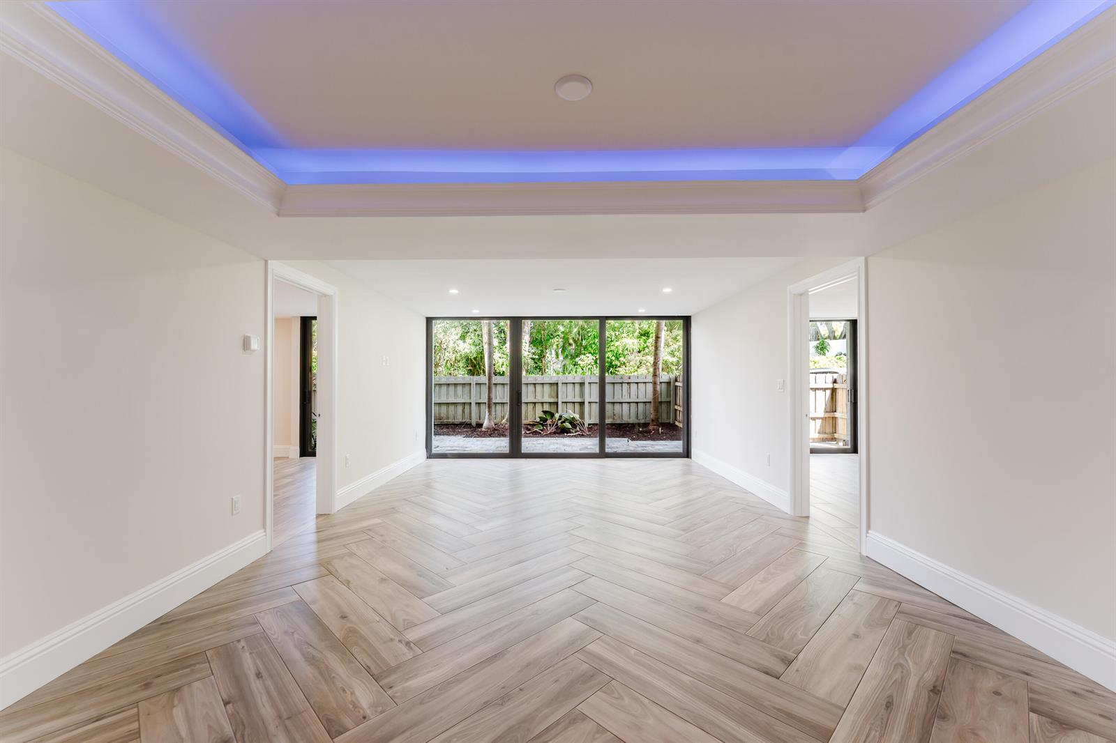 An empty room features herringbone wood-look flooring, a blue tray ceiling, and large glass doors — 501 SW 11th Place # 114, Boca Raton FL 33432, BOCA RATON, FL
