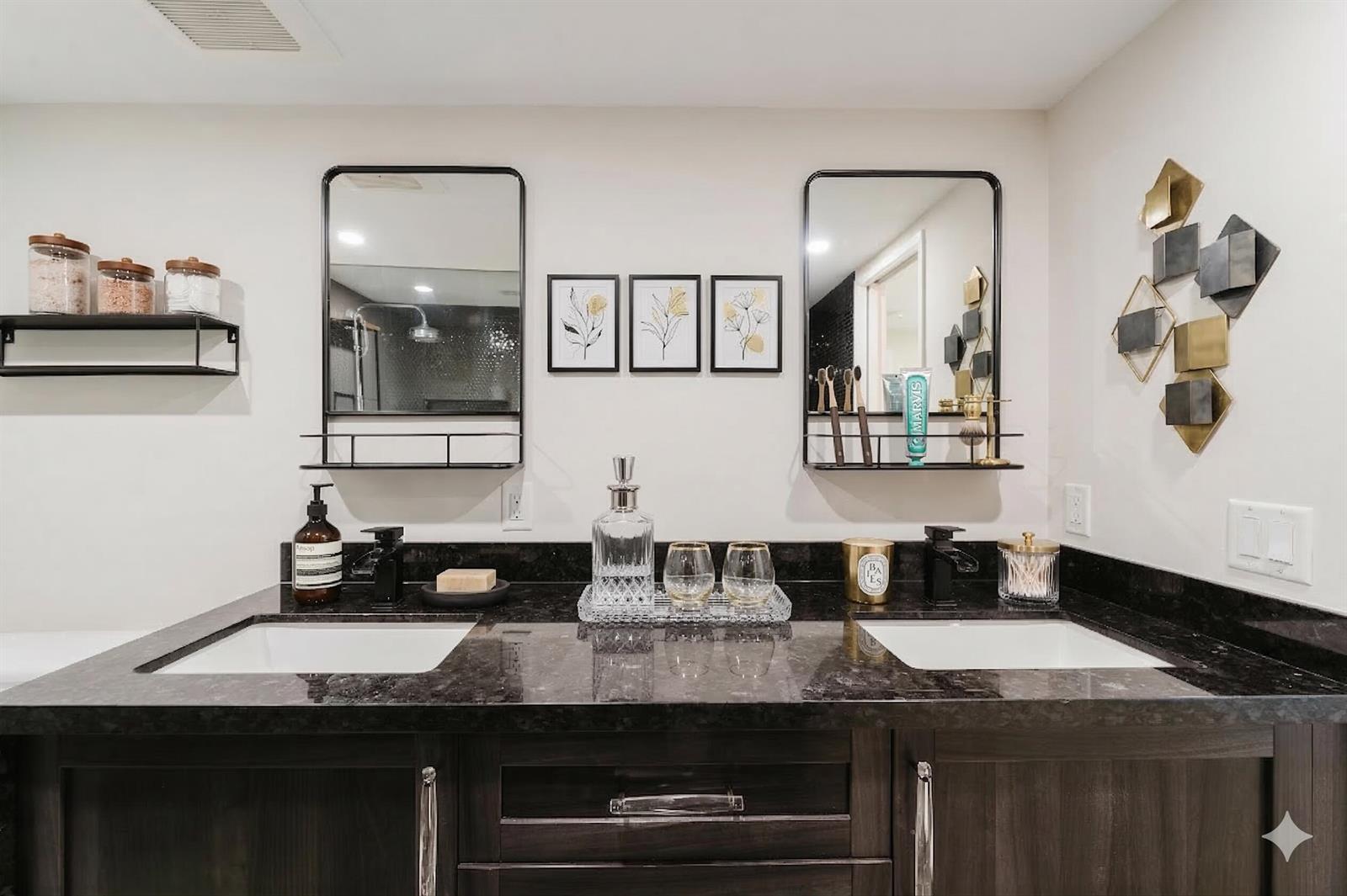 A bathroom vanity features a dark stone countertop, dual sinks, black framed mirrors, and dark cabinetry — 501 SW 11th Place # 114, Boca Raton FL 33432, BOCA RATON, FL