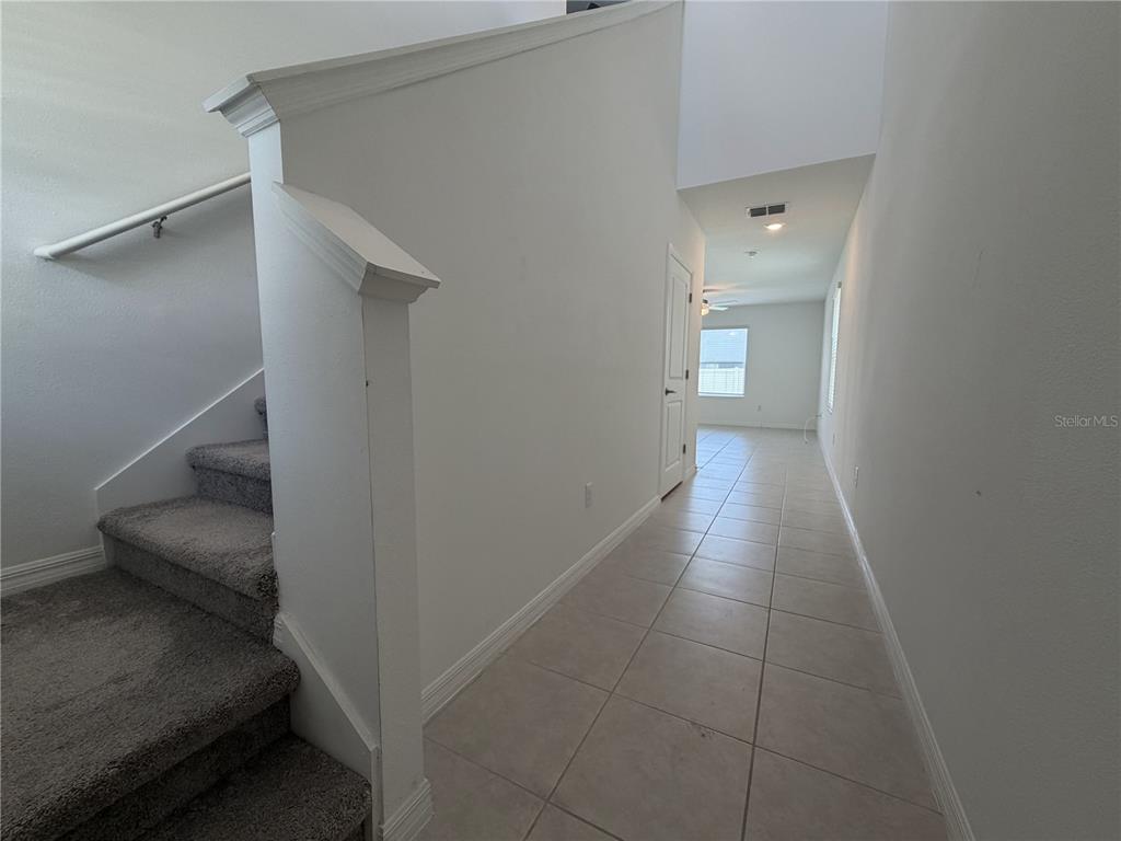 A carpeted staircase sits beside a tiled hallway leading to a room with a window — 156 ROSE BUD LANE, SPRING HILL, FL
