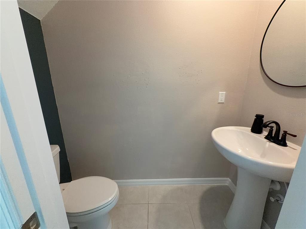 A small bathroom features a pedestal sink, a white toilet, and a round wall mirror — 156 ROSE BUD LANE, SPRING HILL, FL