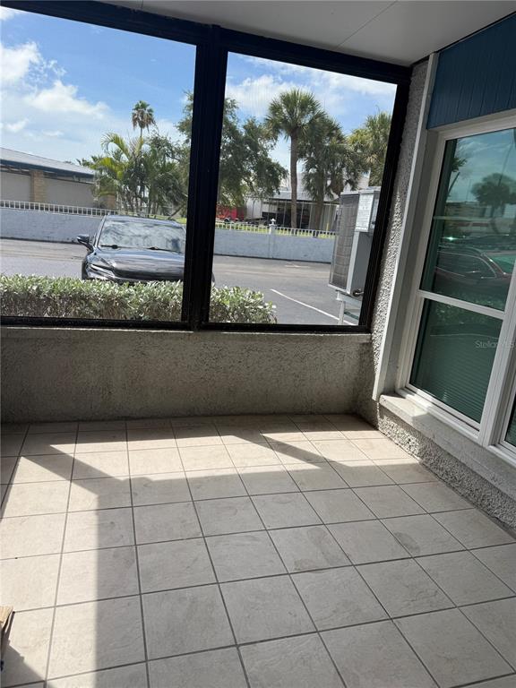 A tiled patio features large windows looking out onto a parking lot and palm trees — 171 MEDALLION BOULEVARD UNIT B, MADEIRA BEACH, FL