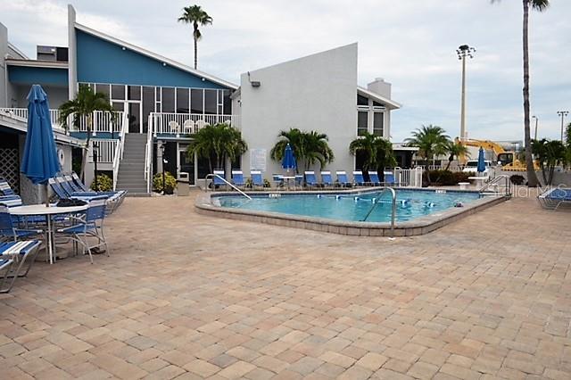 A swimming pool sits on a paved patio in front of a multi-story building — 171 MEDALLION BOULEVARD UNIT B, MADEIRA BEACH, FL