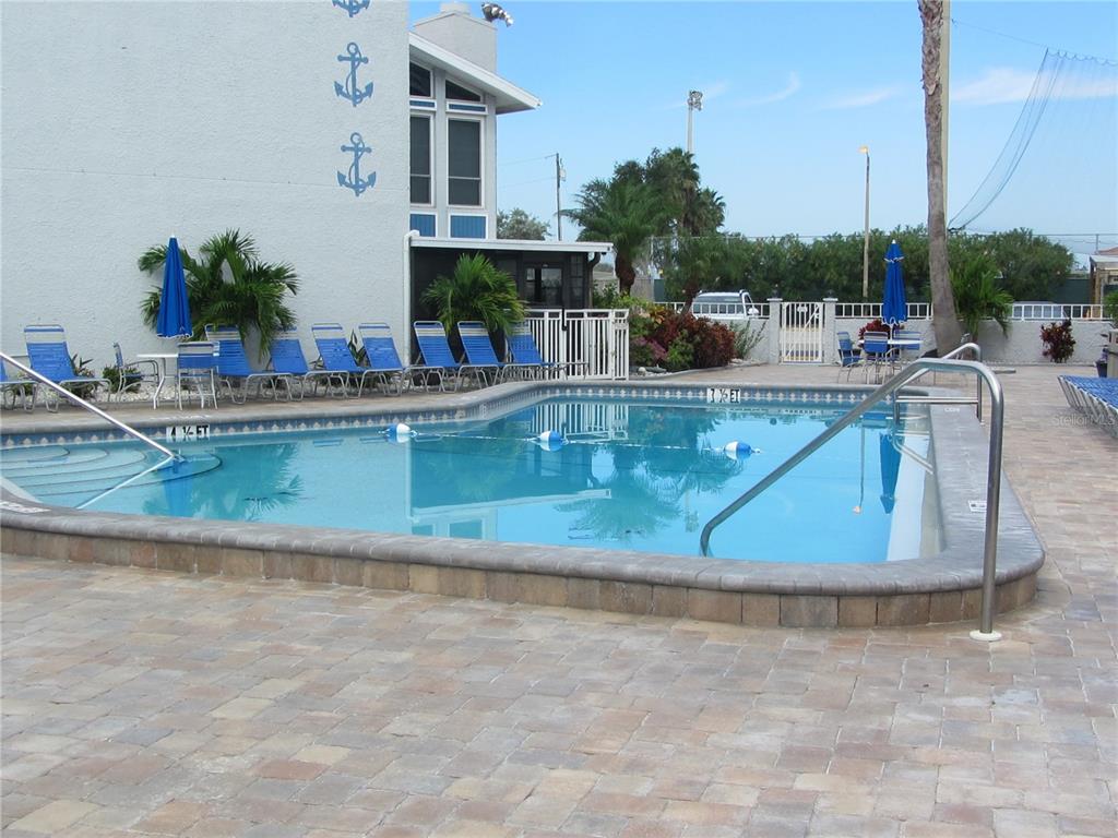 A rectangular swimming pool with a paver deck is situated beside a building with anchors — 171 MEDALLION BOULEVARD UNIT B, MADEIRA BEACH, FL