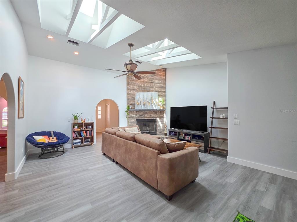 A living room features a brick fireplace, vaulted ceilings with skylights, and gray wood flooring — 126 BIRCHWOOD DRIVE, PALM COAST, FL