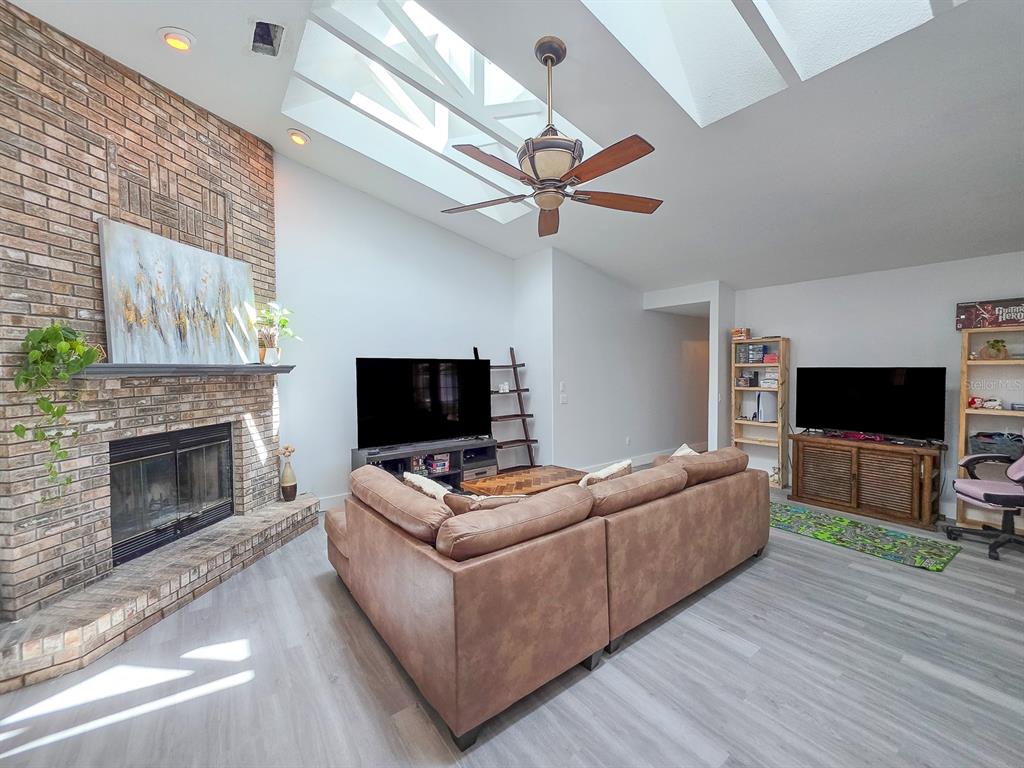 A living room features a brick fireplace, a brown sectional sofa, and a vaulted skylight ceiling — 126 BIRCHWOOD DRIVE, PALM COAST, FL