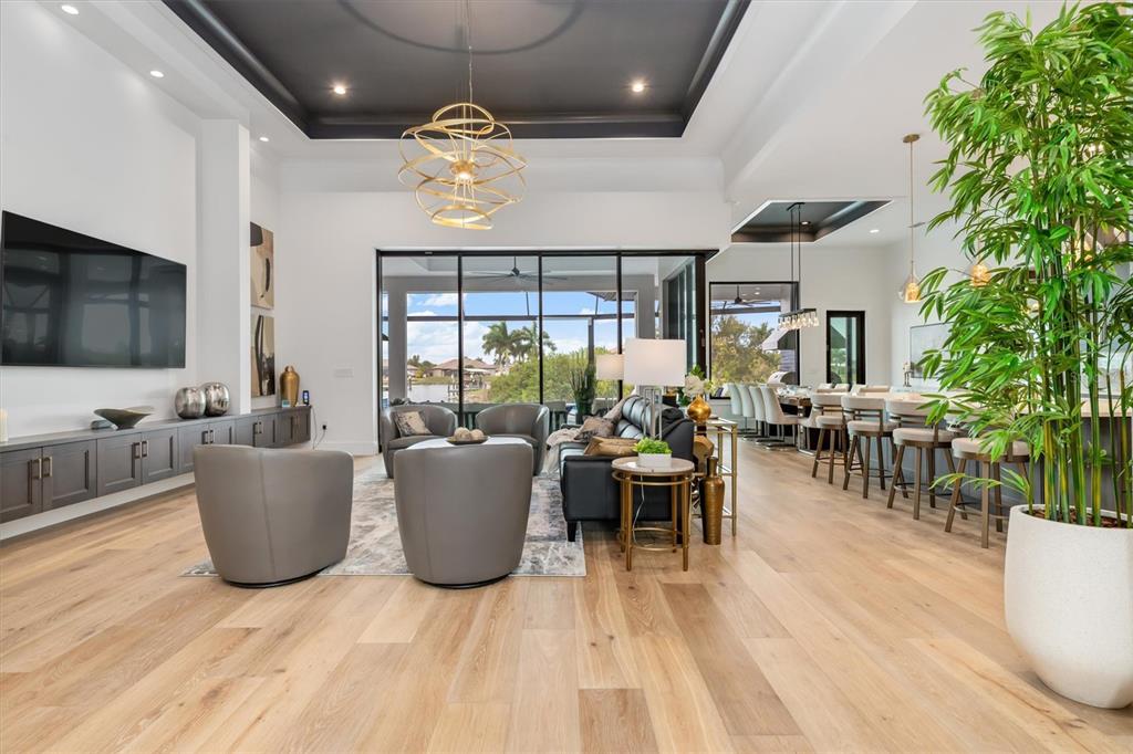 A modern open-concept living room features light wood floors, a dark tray ceiling, and glass walls — 9474 MELODY CIRCLE, PORT CHARLOTTE, FL