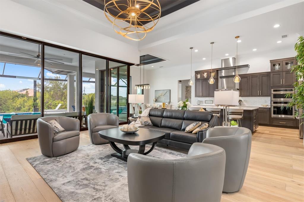 An open-concept living room and kitchen featuring a black leather sofa, gray armchairs, and pool views — 9474 MELODY CIRCLE, PORT CHARLOTTE, FL