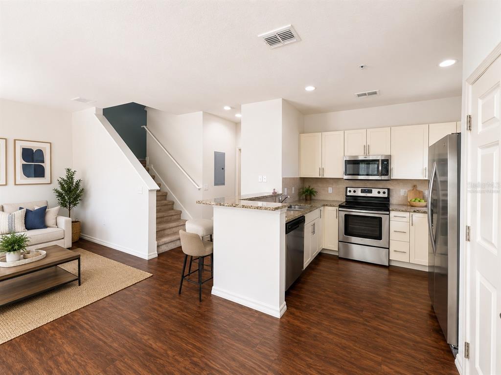 An open-concept kitchen with stainless steel appliances and granite countertops overlooks a living area — 3208 OYSTER LANE, KISSIMMEE, FL