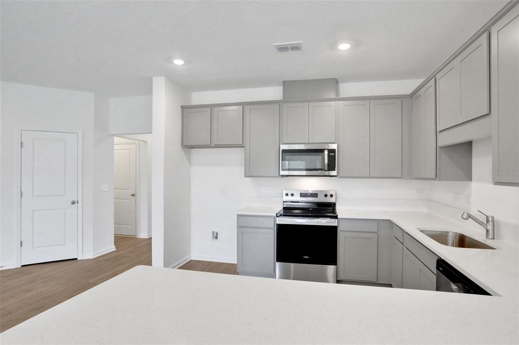 A kitchen features light gray cabinets, white countertops, stainless steel appliances, and wood-look flooring — 5792 LAGOON CRUISE WAY, JACKSONVILLE, FL