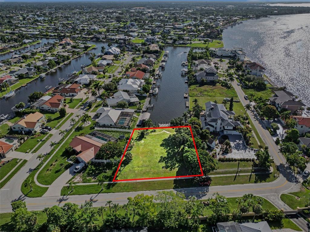 An aerial view shows a vacant, rectangular residential lot outlined in red near a canal — 180 COUSLEY DRIVE SE, PORT CHARLOTTE, FL