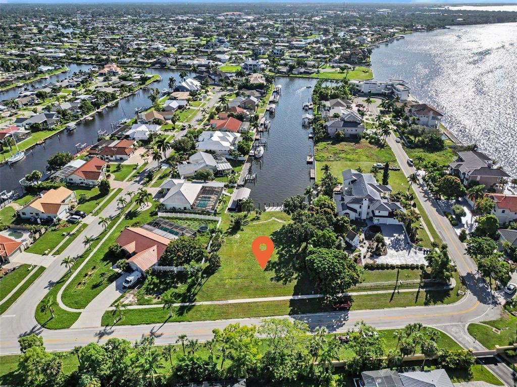 An aerial view shows a vacant waterfront lot marked with a pin in a neighborhood — 180 COUSLEY DRIVE SE, PORT CHARLOTTE, FL