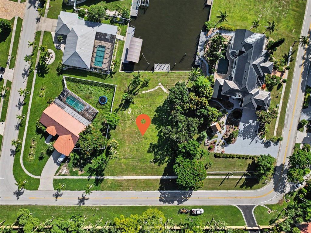 An aerial view shows a vacant waterfront lot situated between two large residential properties — 180 COUSLEY DRIVE SE, PORT CHARLOTTE, FL
