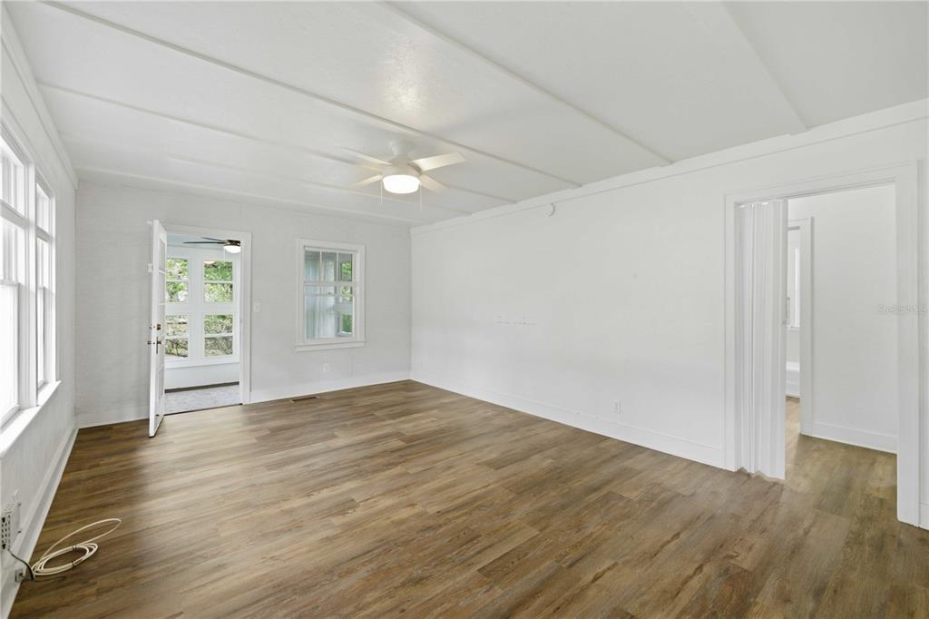 A bright, empty room features white walls, wood-look flooring, and a ceiling fan — 923 NE 2ND STREET, OCALA, FL