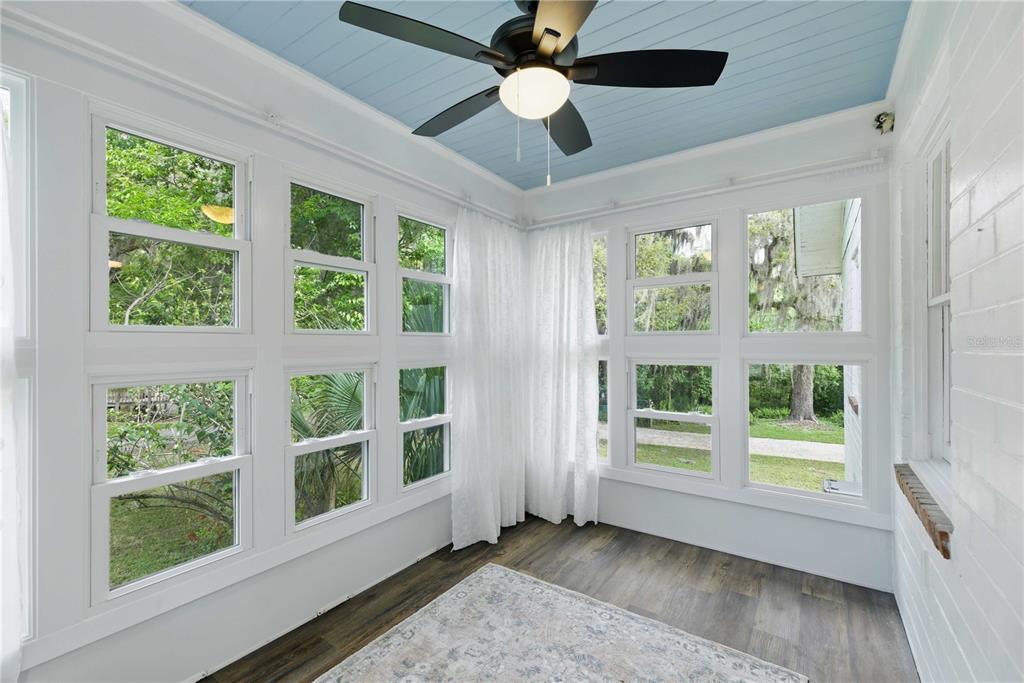 A sunroom with white walls, a light blue ceiling, wood-look flooring, and many windows — 923 NE 2ND STREET, OCALA, FL